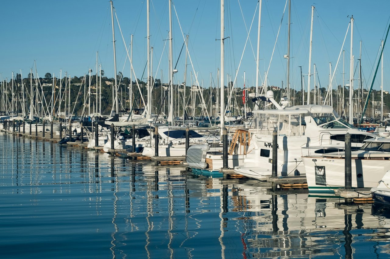 Sailboats and motorboats fill a marina, reflected in calm water beneath a clear blue sky.