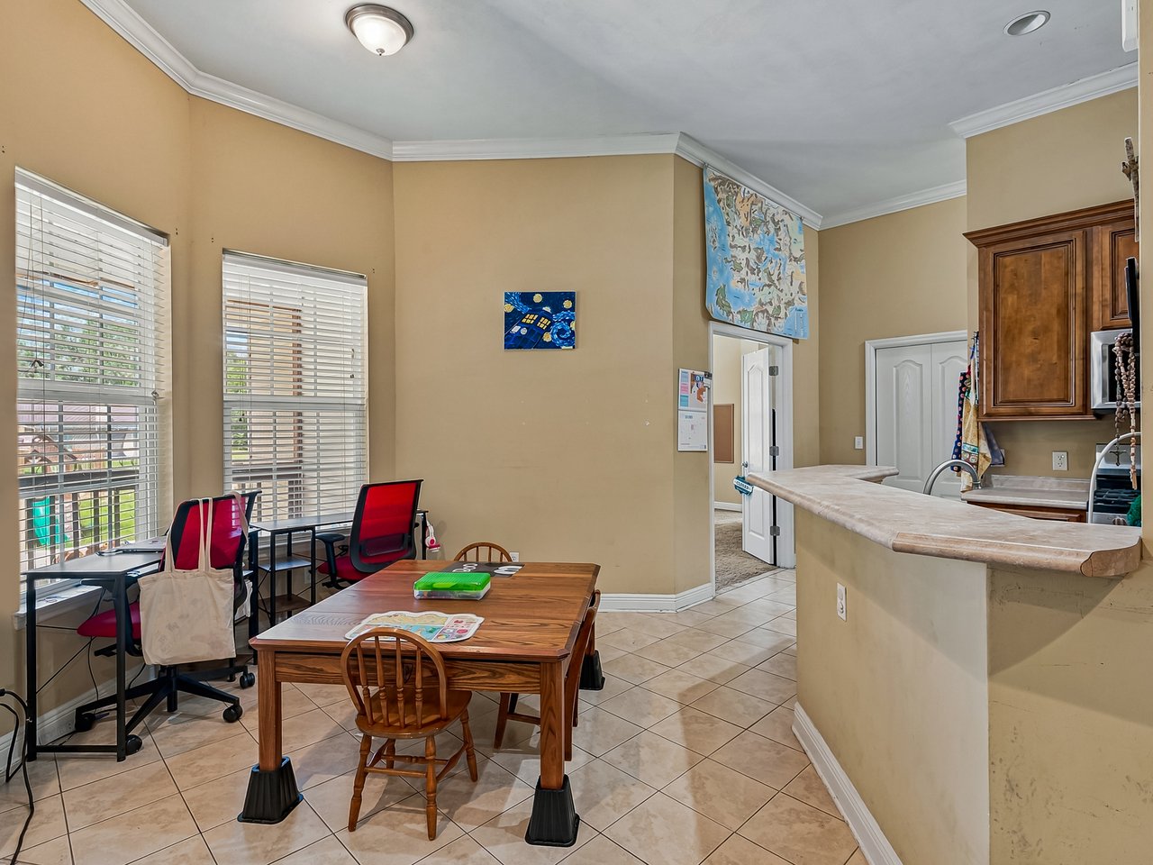 Dining area with a wooden table, large windows, tiled floor, and curved kitchen breakfast bar.