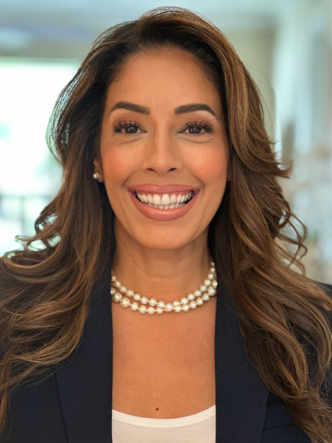 Lissette Lozada smiling in a navy blazer and pearl necklace.