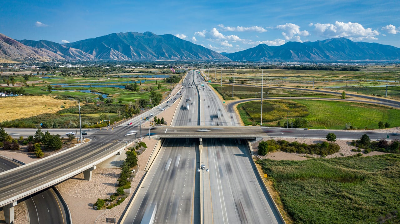 Aerial view of a Utah County freeway interchange with mountains and open farmland in the background