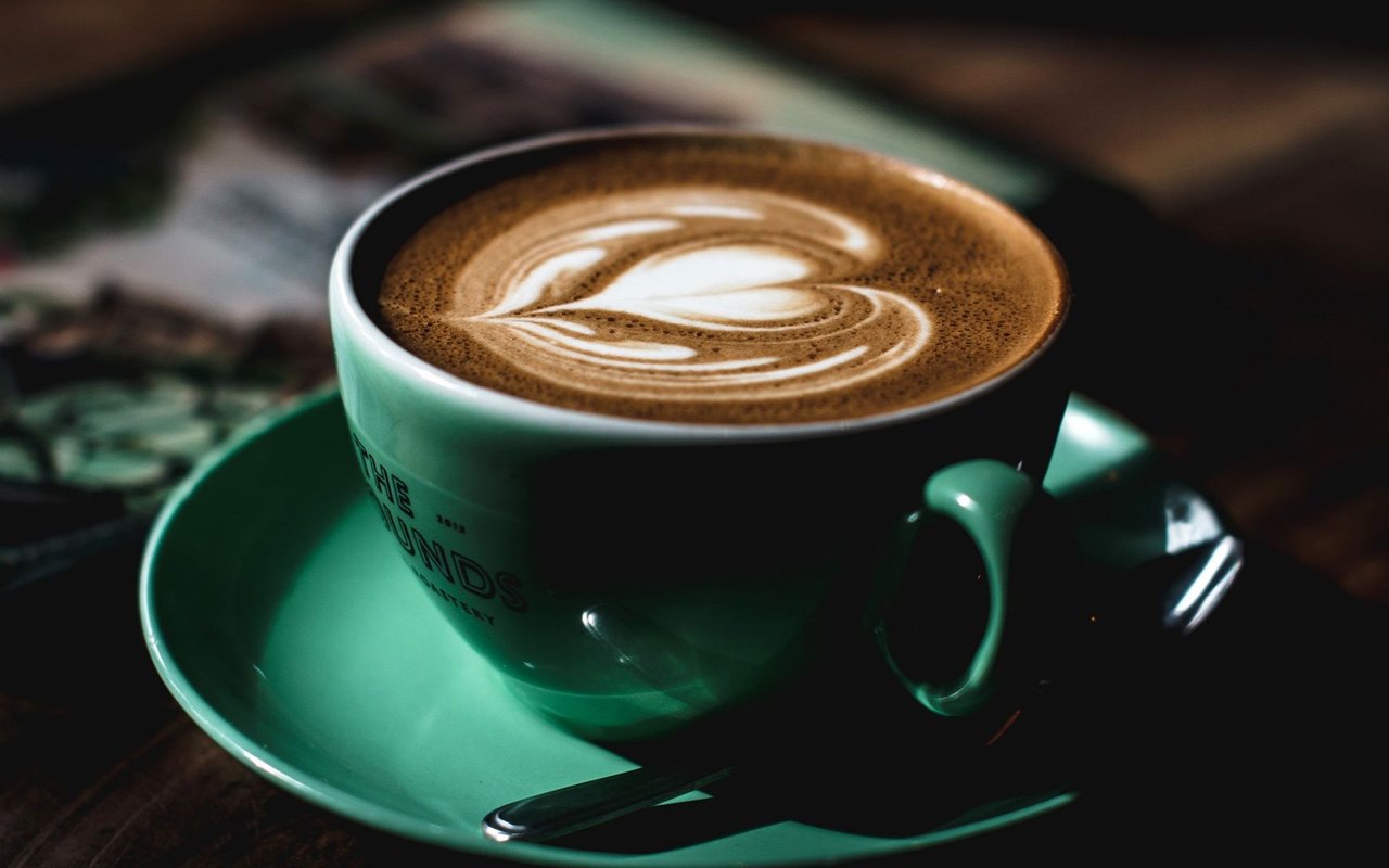 Latte with leaf-shaped foam art in a turquoise cup and saucer.