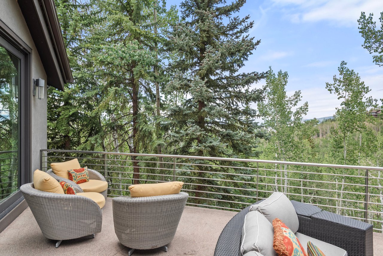Furnished balcony with wicker lounge chairs overlooking evergreen and aspen trees.