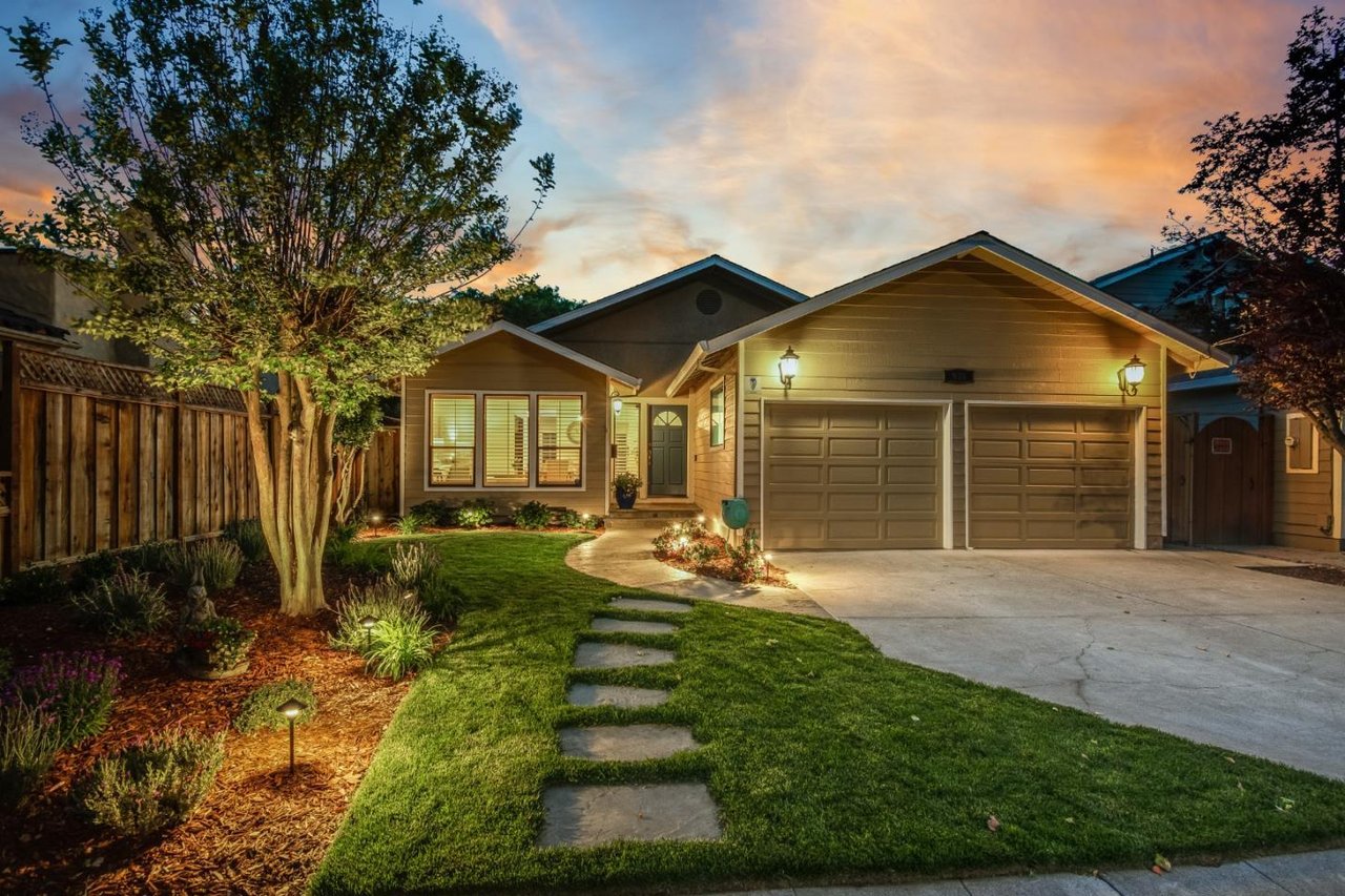 Single-story home with a two-car garage, warmly lit windows, and a stepping-stone path across the lawn.