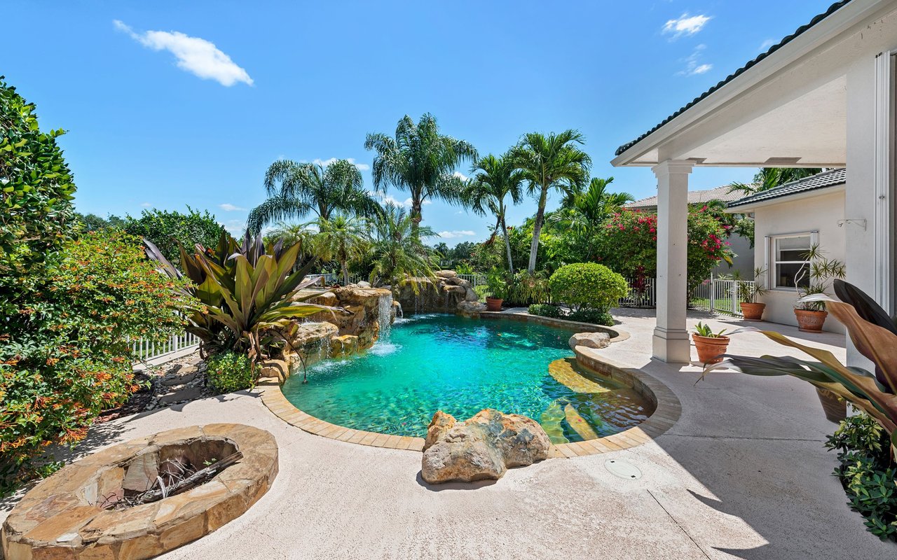 Freeform swimming pool with a rock waterfall beside a covered patio and tropical palms.