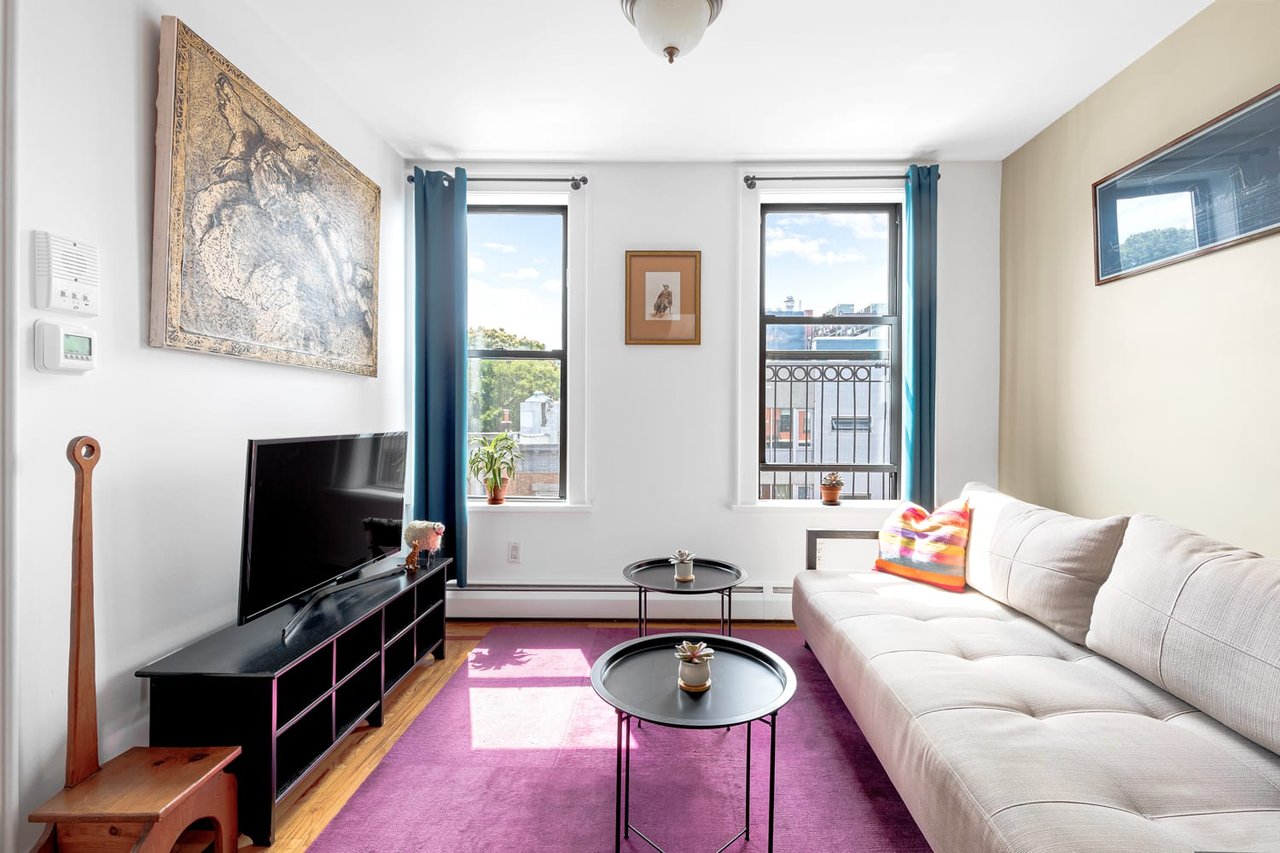 Living room with a white sectional, purple rug, and two sunny windows.