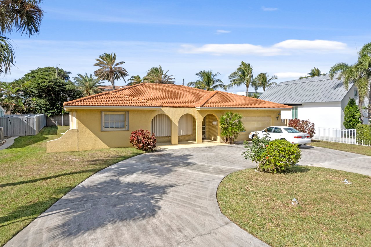 Single-story yellow stucco home with a terracotta tile roof, arched entryways, and a curved driveway.