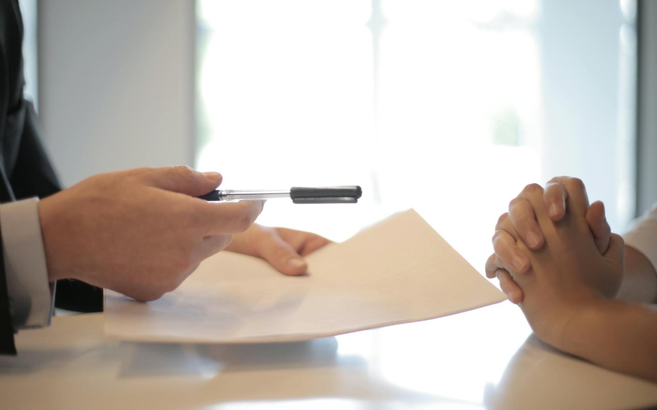 People discuss paperwork at a table, with a pen poised over a document.