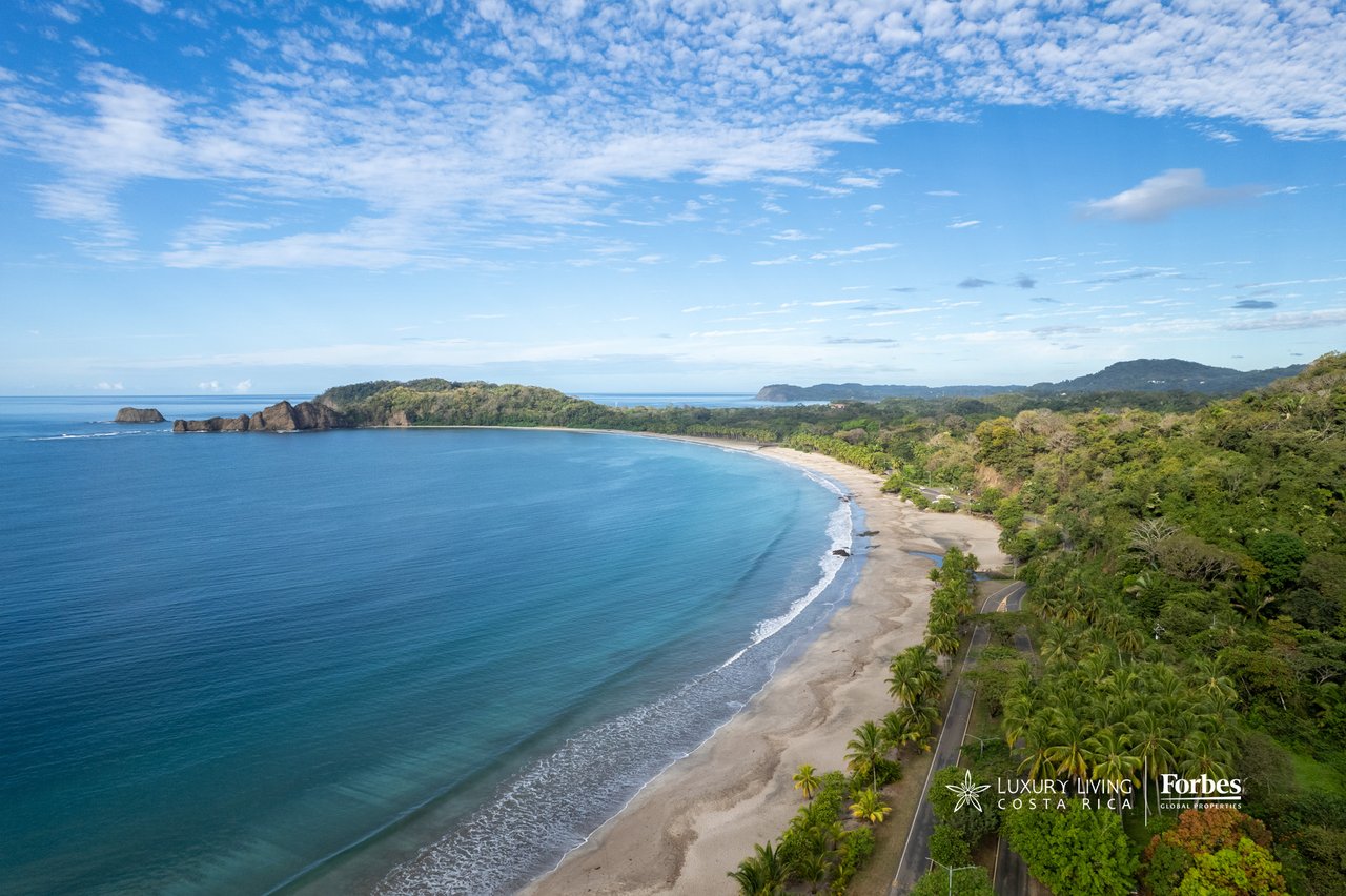 Aerial view of a curving Costa Rican beach, turquoise bay, and forested coastline.