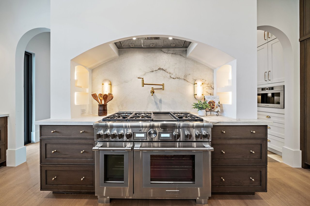 Luxury kitchen with a stainless-steel range, veined marble backsplash, and brass pot filler.