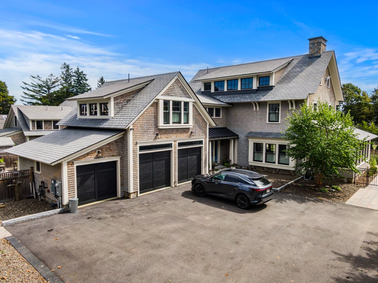Shingle-style home with multiple garage doors and a dark car in the driveway.