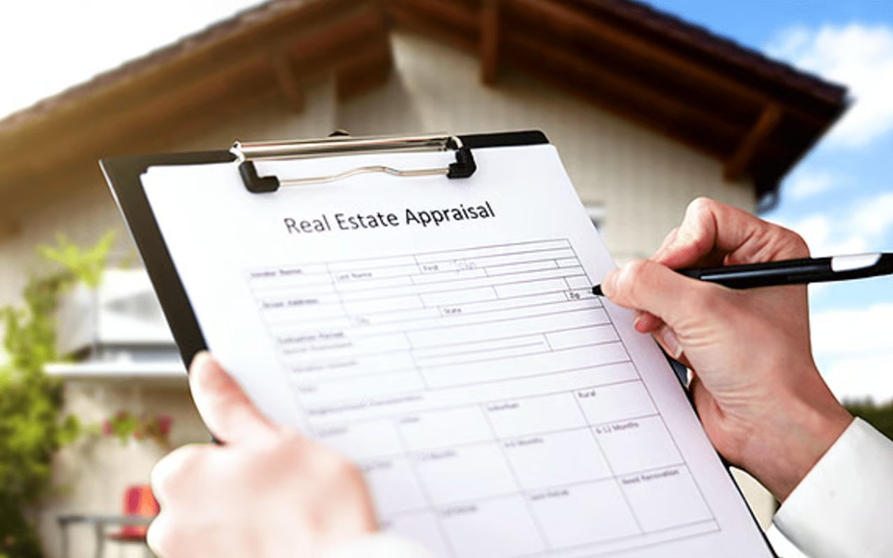 Hands writing on a real estate appraisal form in front of a house.