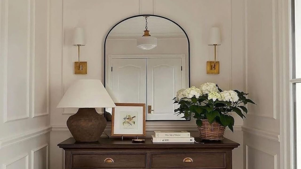 Foyer console with an arched mirror, brass sconces, and white flowers.