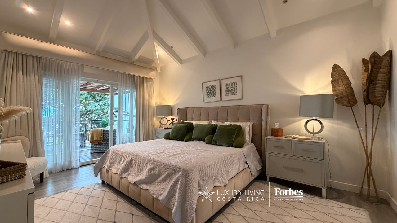Furnished bedroom with a large bed beneath a vaulted ceiling and sliding doors to a patio.