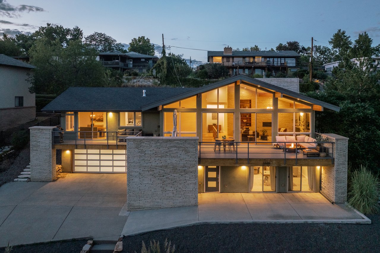 Modern home at dusk with a glass gabled facade and a warmly lit balcony terrace.