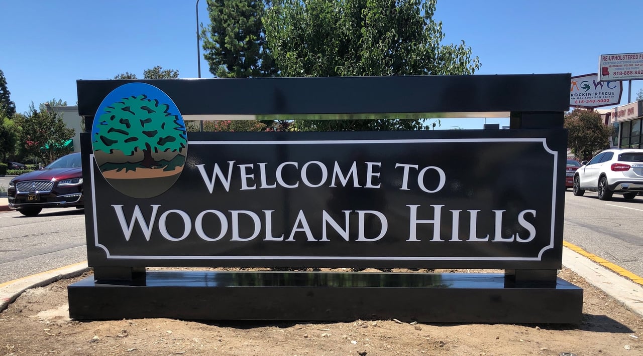 A large wooden monument sign that reads Welcome to Woodland Hills on a sunny day.