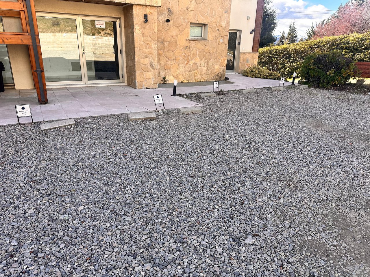 Apartment entrance with a tan stone facade, glass doors, and a gravel forecourt.