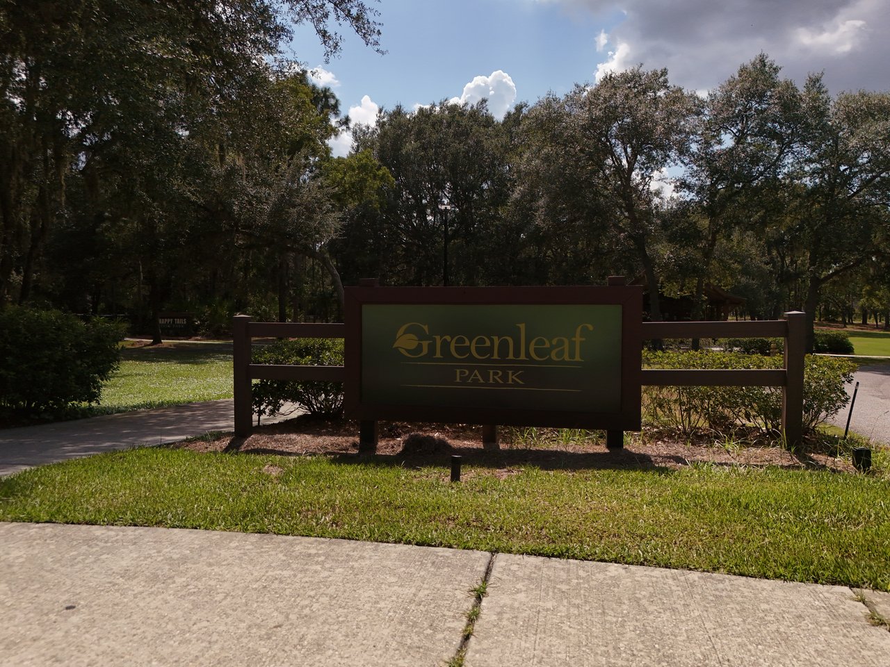 Greenleaf Park entrance sign amid mature trees and landscaped grounds.