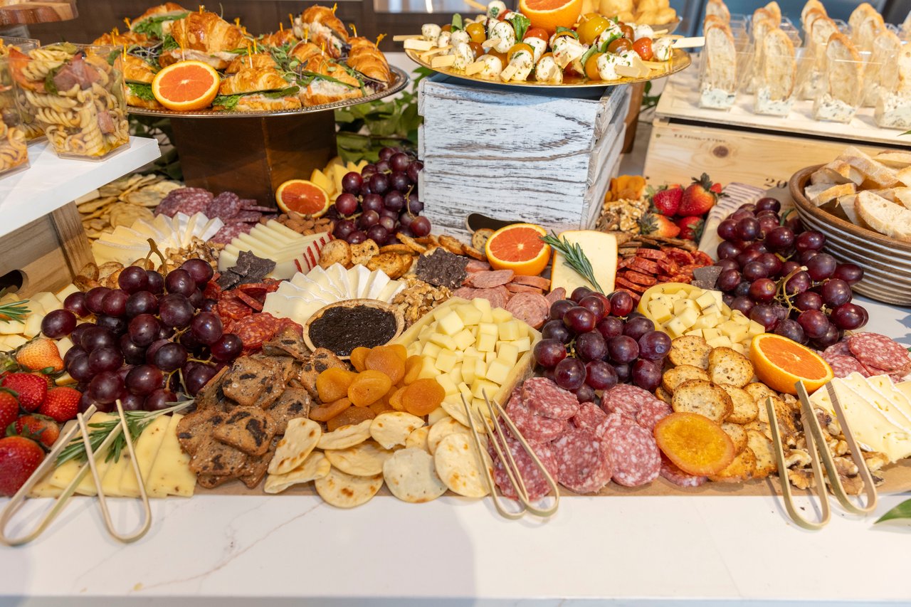 A buffet spread of cheeses, cured meats, grapes, berries, crackers, and skewered appetizers.