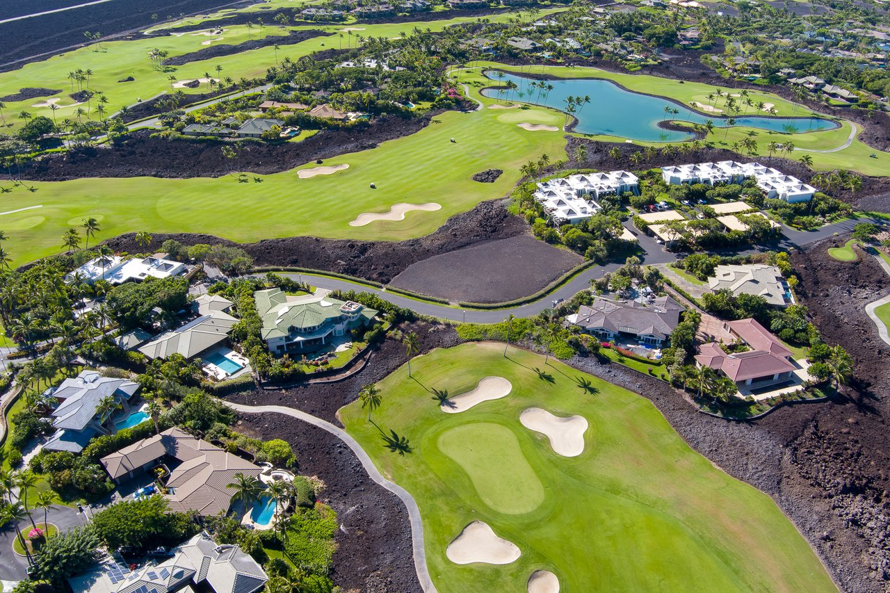 Aerial view of homes beside a golf course and lagoon in a lush coastal community.