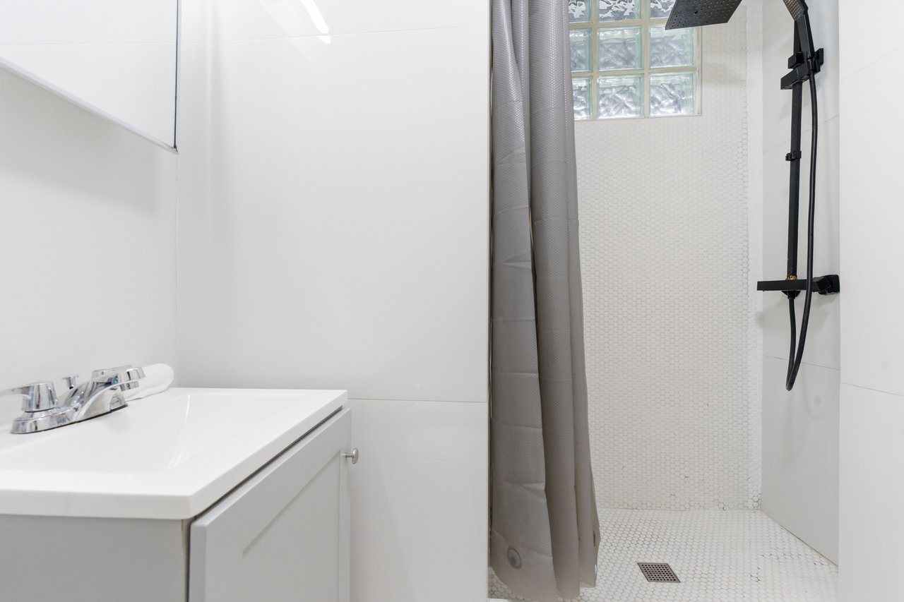 Bathroom with a white vanity and tiled walk-in shower, gray curtain, and glass-block window.
