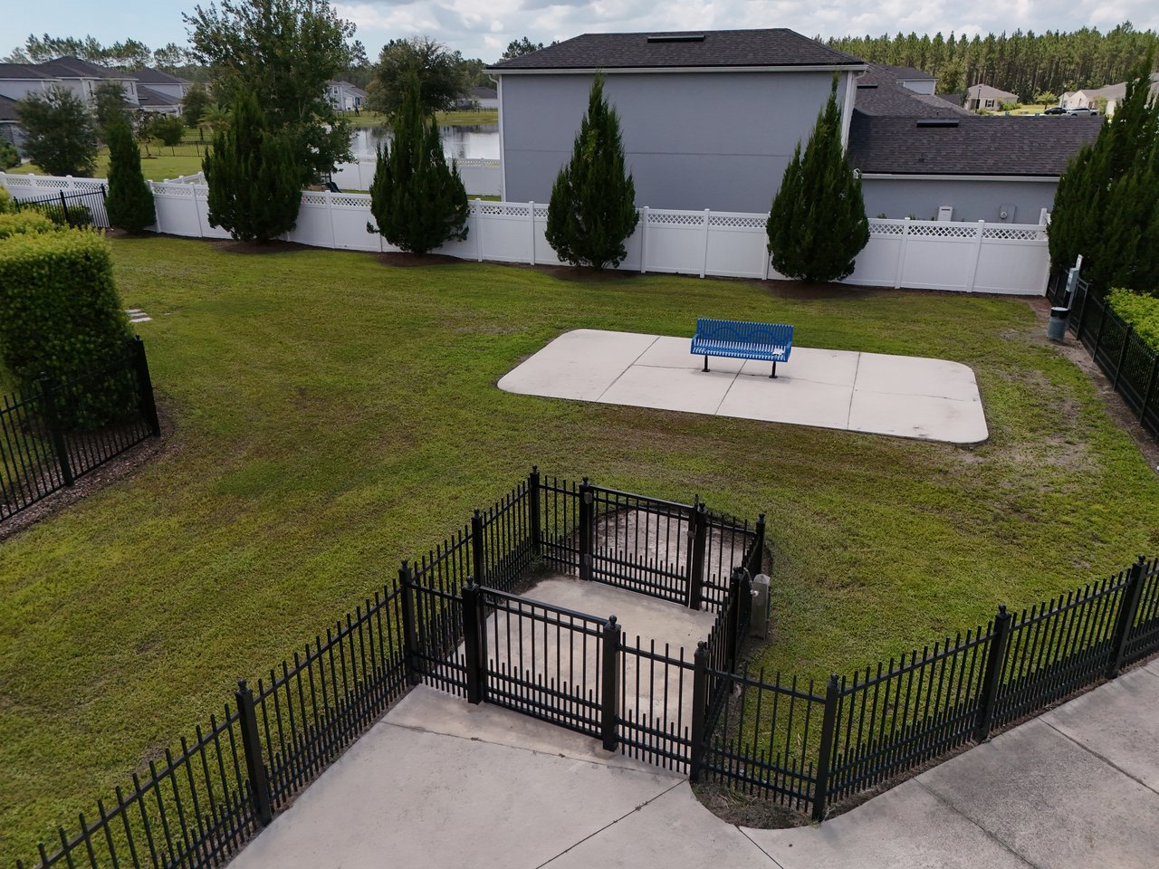 Fenced grassy community area with a blue bench and pond visible behind the white fence.