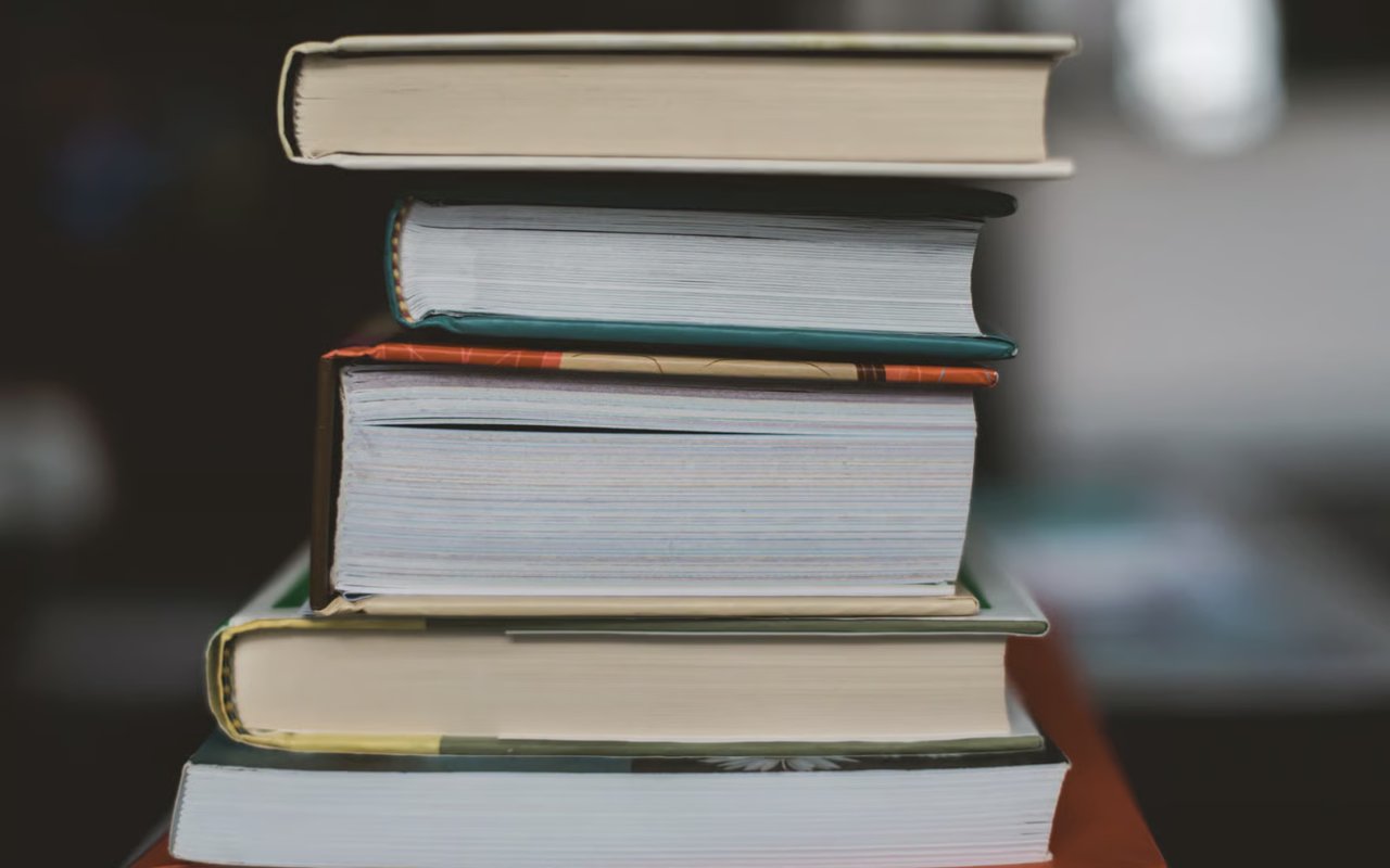 A close-up, stacked shot of five hardcover books, showing the worn and different colored pages.