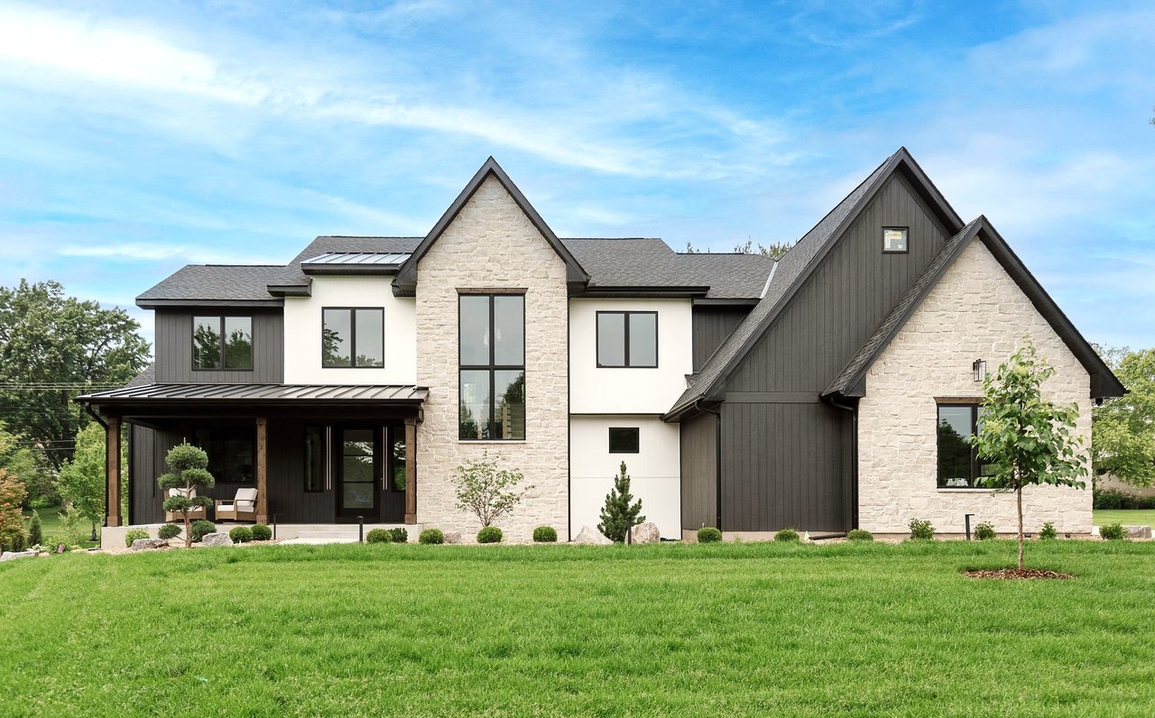 Modern stone-and-dark-siding house with steep gables, a covered porch, and a broad green lawn.