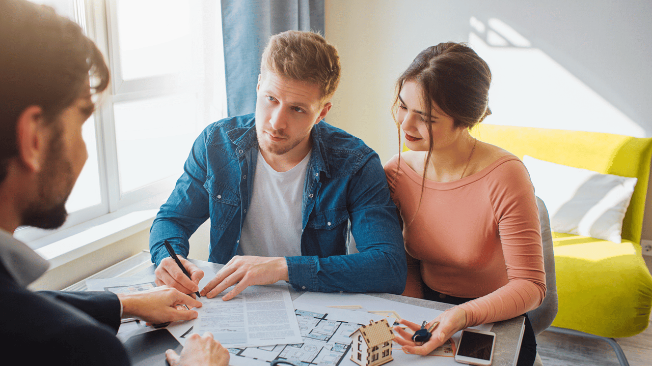 A couple reviews home-buying paperwork and floor plans with a real estate professional.