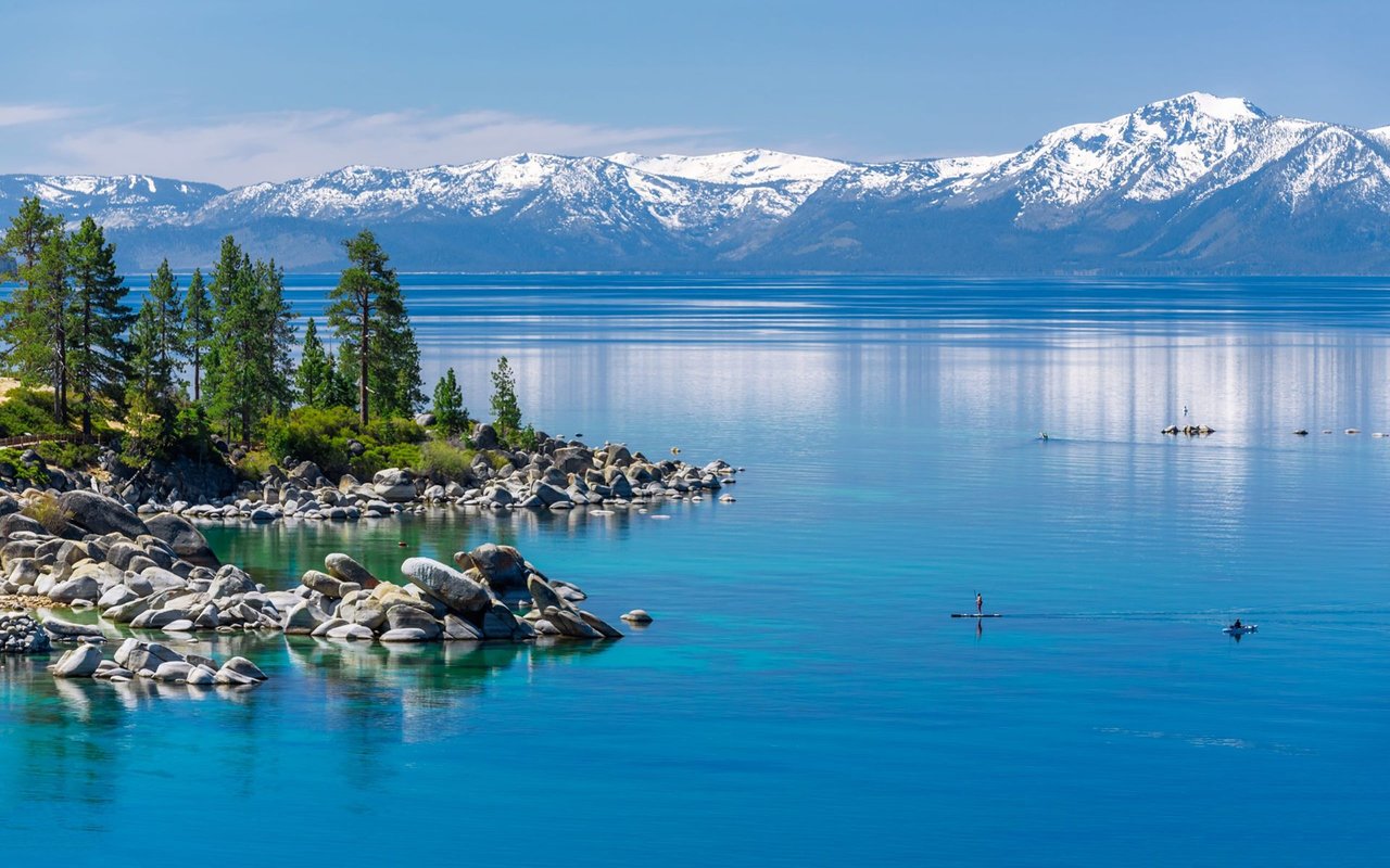 Lake Tahoe and its rocky pine shoreline, with snow-covered Sierra Nevada mountains beyond.