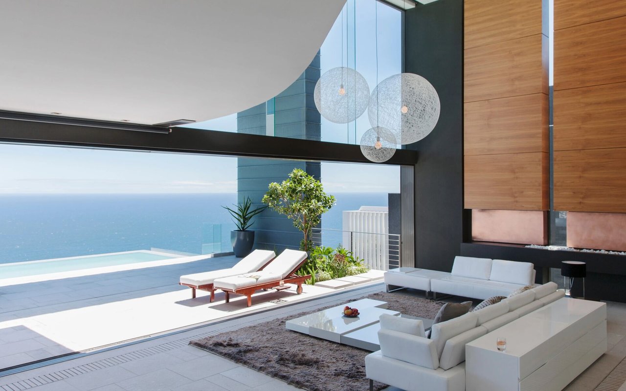 Modern living room opens onto an ocean-view terrace with a pool and white lounge furniture.