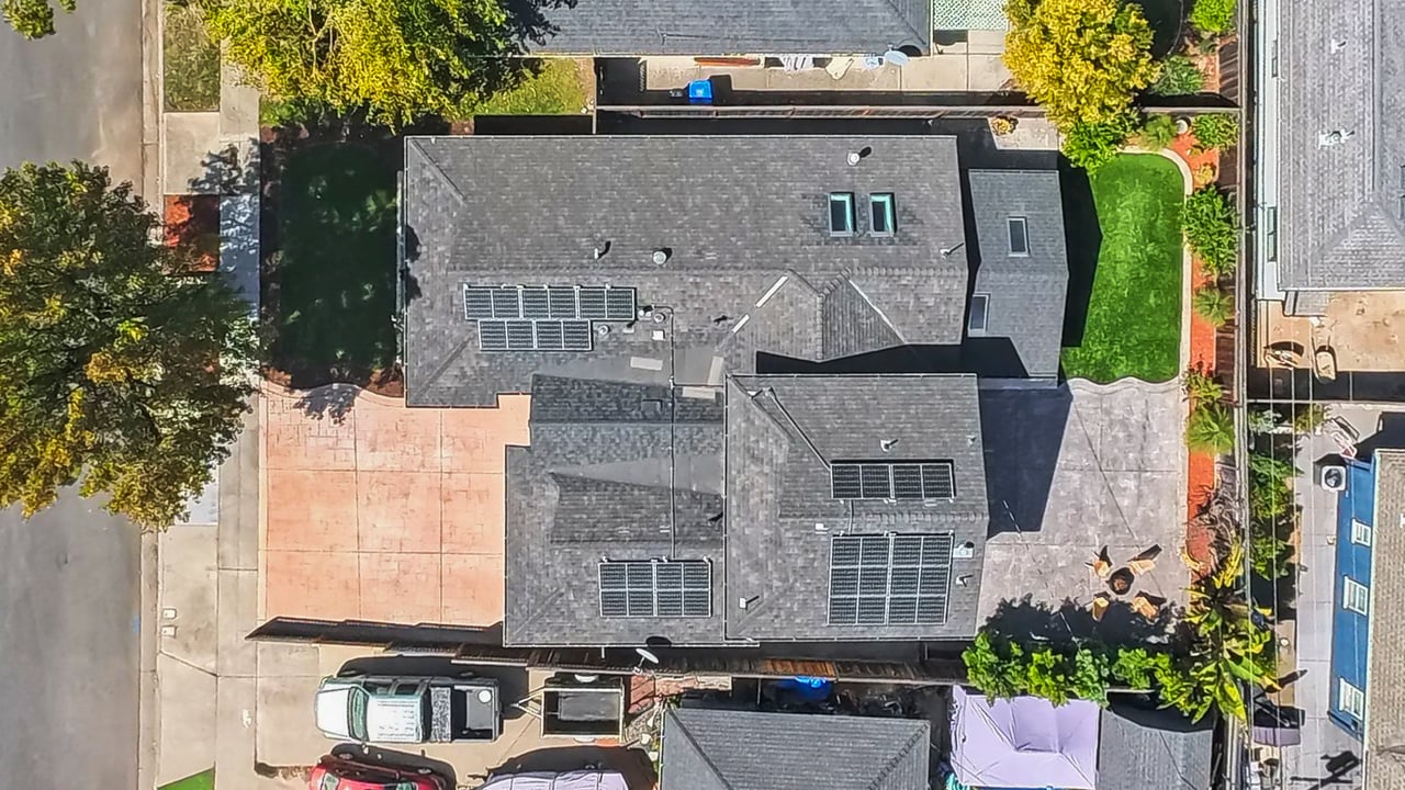 Aerial view of a house with rooftop solar panels, a paved driveway, and a small lawn.