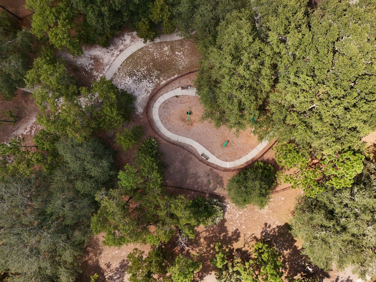 Aerial view of a wooded community park with a curved path and small play area.