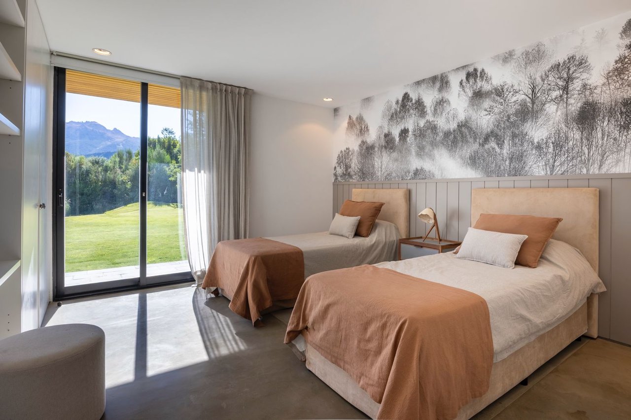 Bedroom with two beds, a forest mural, and sliding doors overlooking a lawn and mountains.