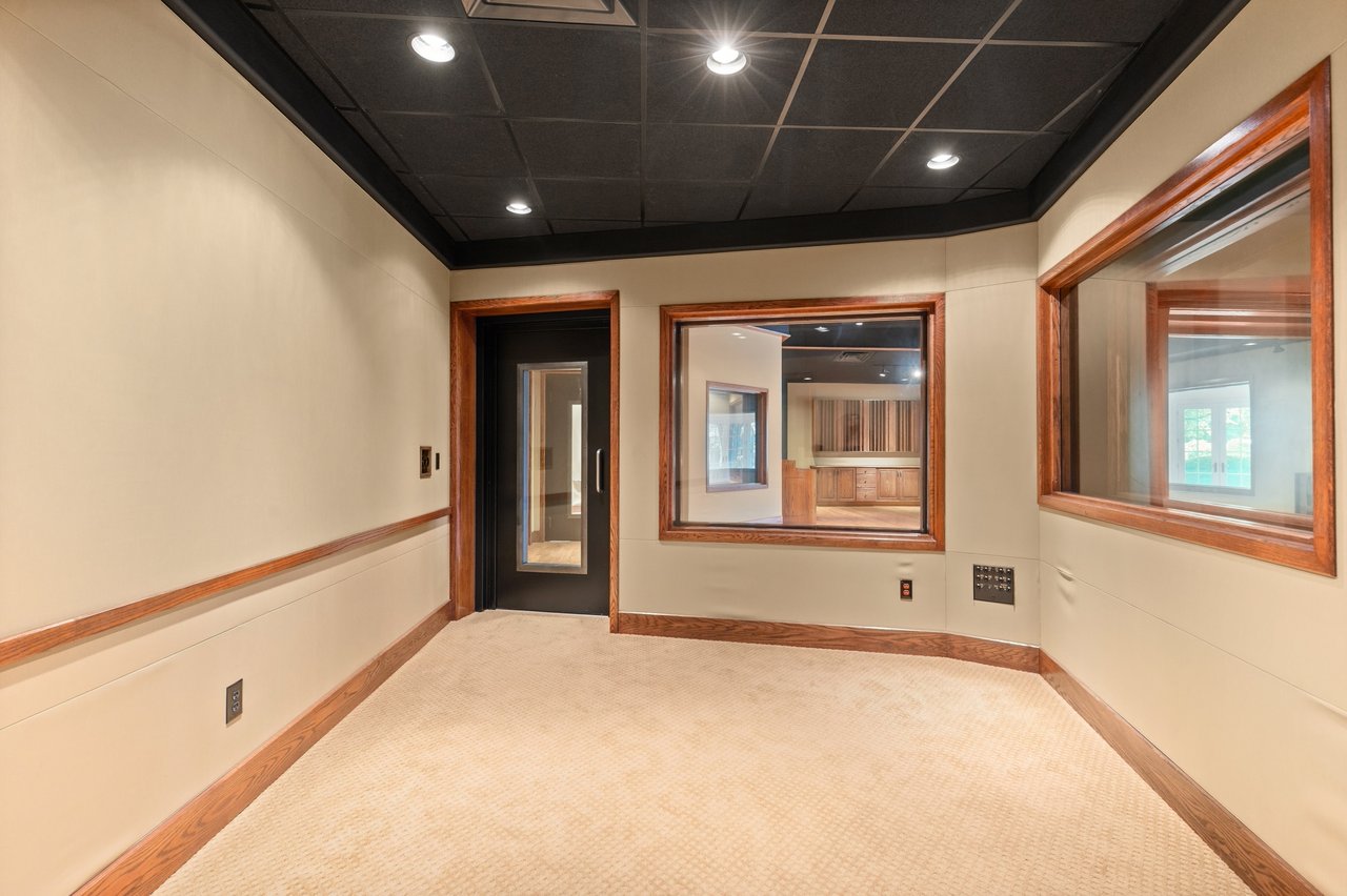 Empty music studio with a dark grid ceiling and wood-trimmed interior windows.