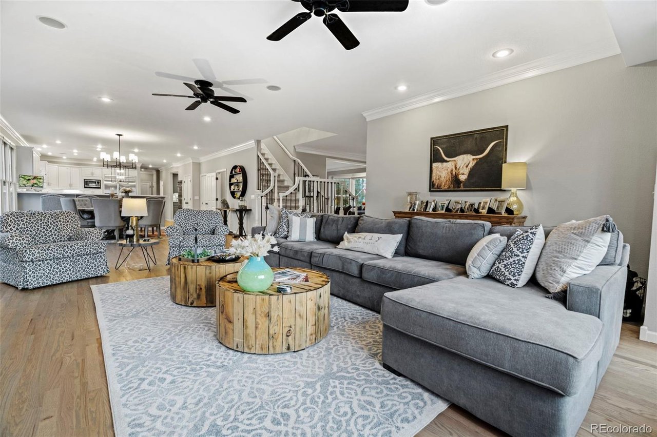 Open-plan living room with a gray sectional, round wood coffee tables, and kitchen beyond.