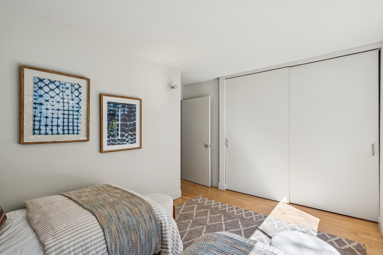 Contemporary bedroom with framed textile art, a patterned bedspread, and large white sliding closet doors.