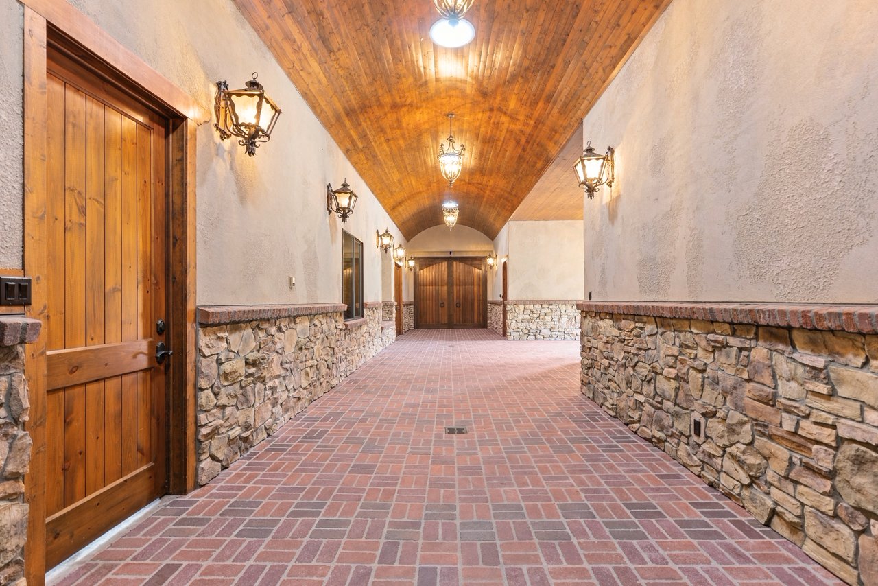 Barn passage with a vaulted wood ceiling, brick floor, stone walls, and wooden doors.