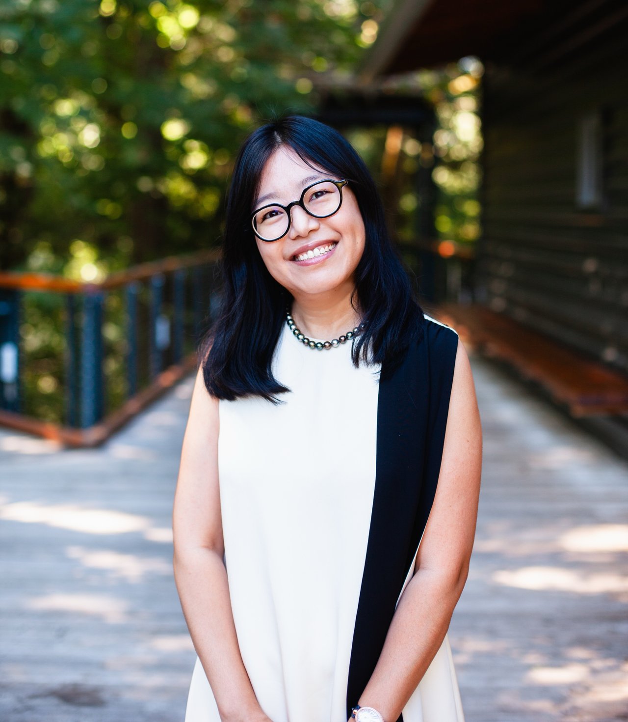 Sheryl Yang smiling in round glasses and a black-and-white sleeveless outfit.