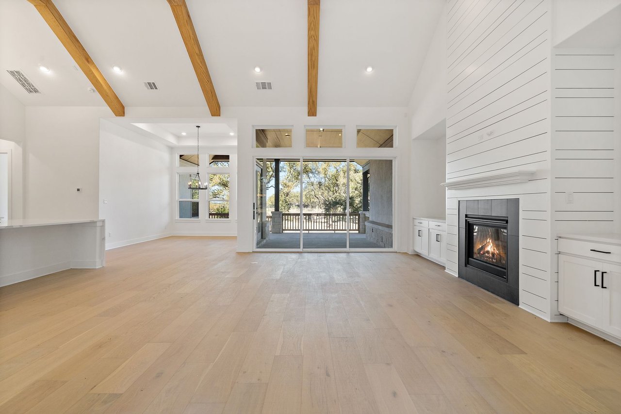 Family room with an exposed wood beam ceiling, a gas fireplace with a shiplap surround, and a wall of windows in the Cortaro home at 133 Mataro Cove, Dripping Springs, Texas.