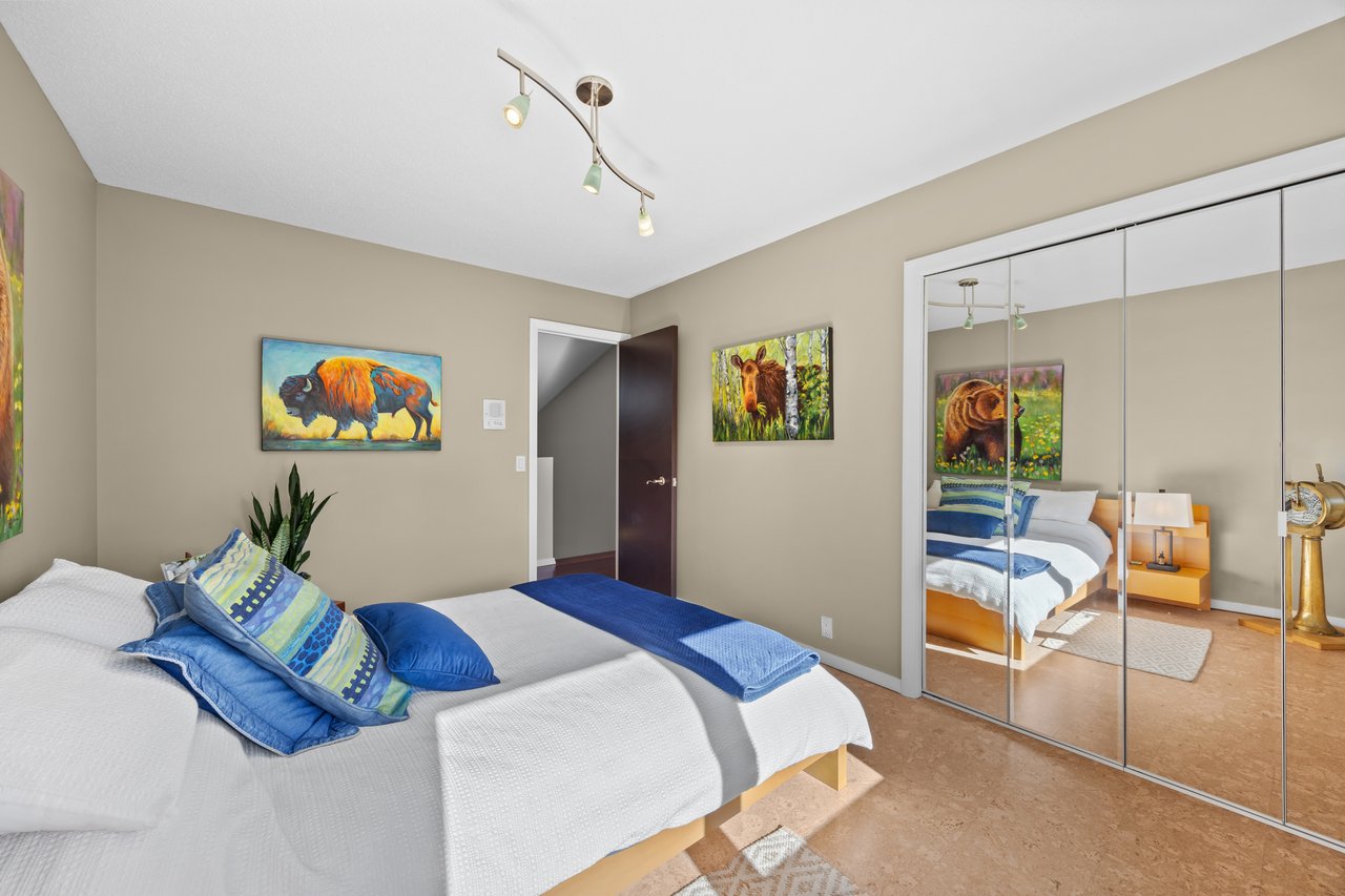 Bedroom with white bedding, blue accent pillows, mirrored closet doors, and wildlife paintings.