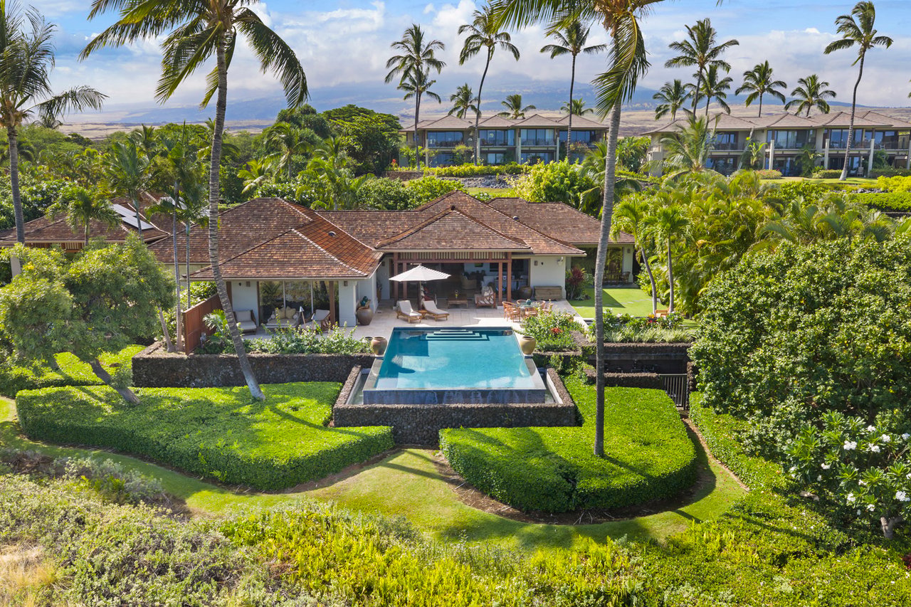 Tropical home with a red-tile roof, rectangular pool, and palm-lined gardens.