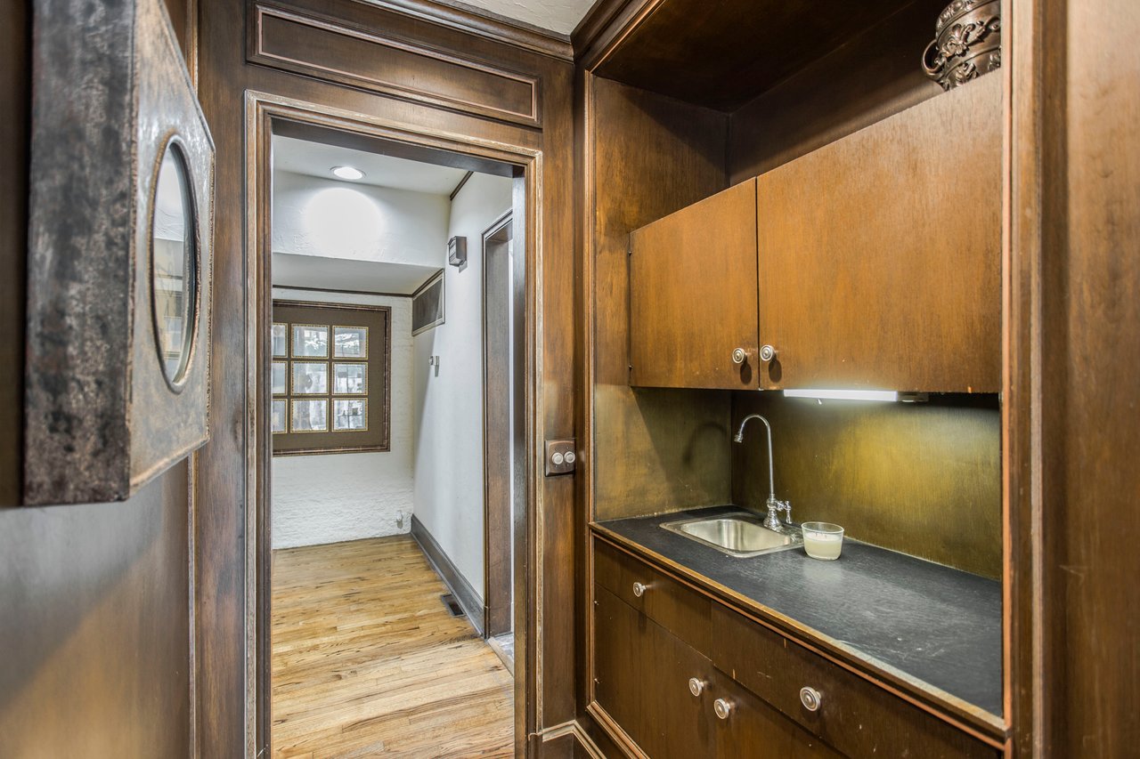 Built-in wood kitchenette with a sink, viewed beside a doorway to a hardwood-floored hall.