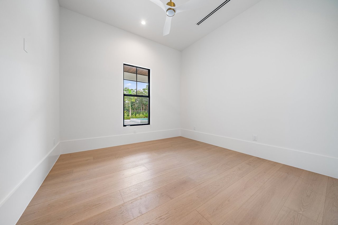 Empty room with light wood floors, a tall window, and a ceiling fan.