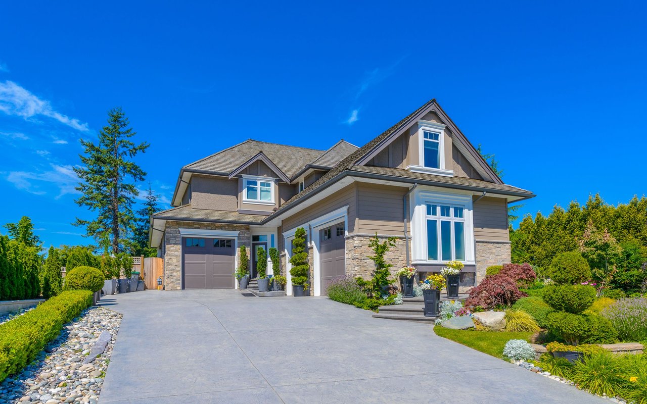 Two-story house with stone accents, a broad driveway, and landscaped flower beds.