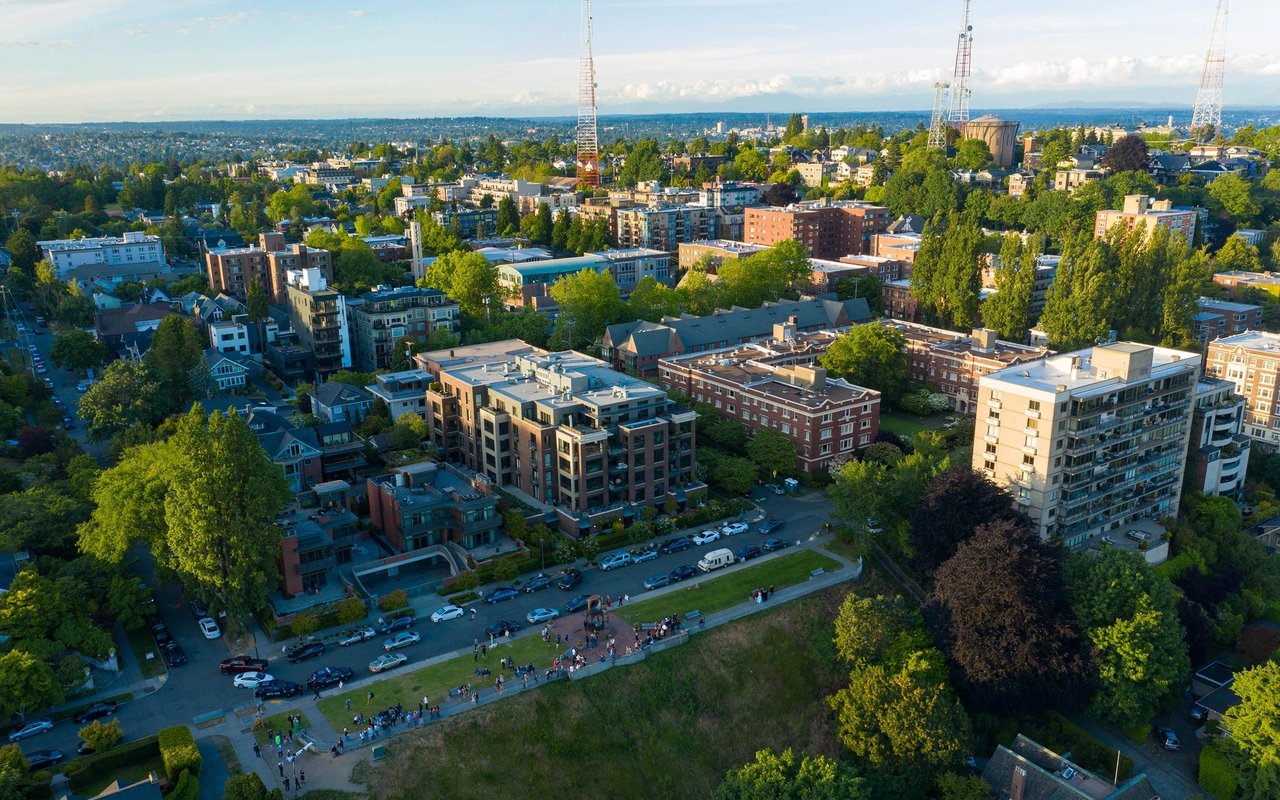 Aerial view of Queen Anne’s tree-lined streets and apartment buildings, with communications towers and distant hills.