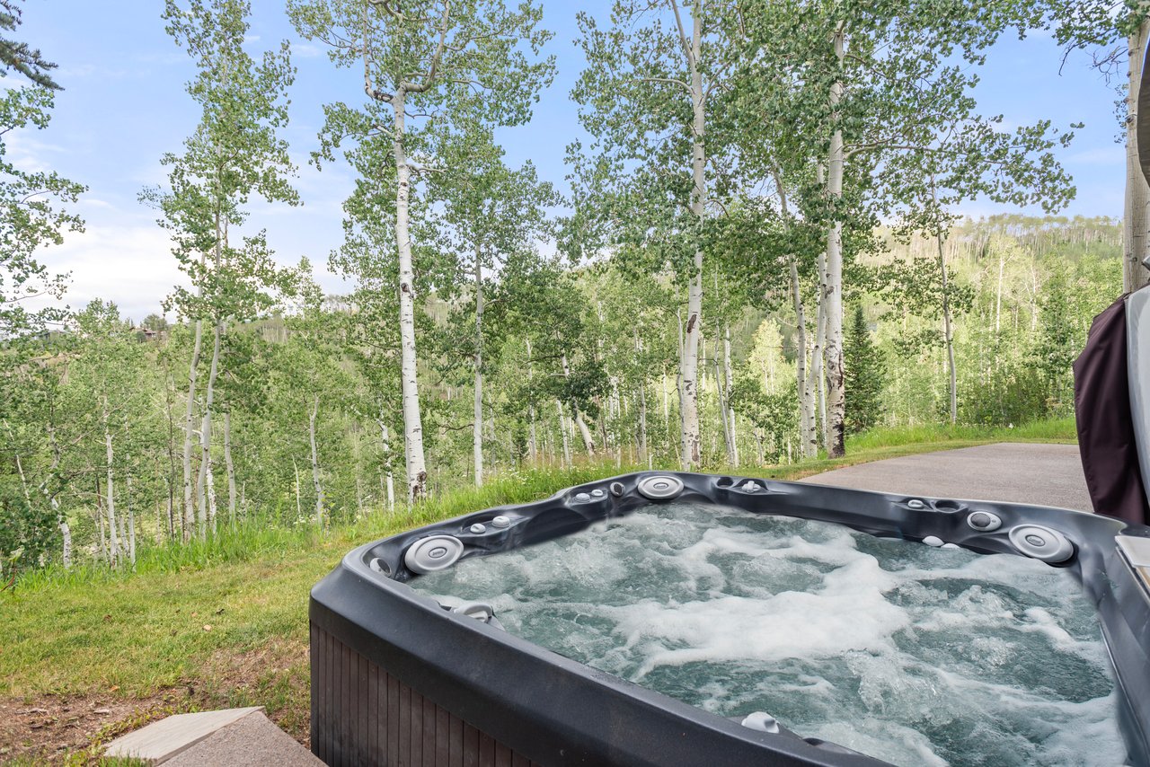Outdoor hot tub bubbling beside an aspen grove on a wooded hillside.