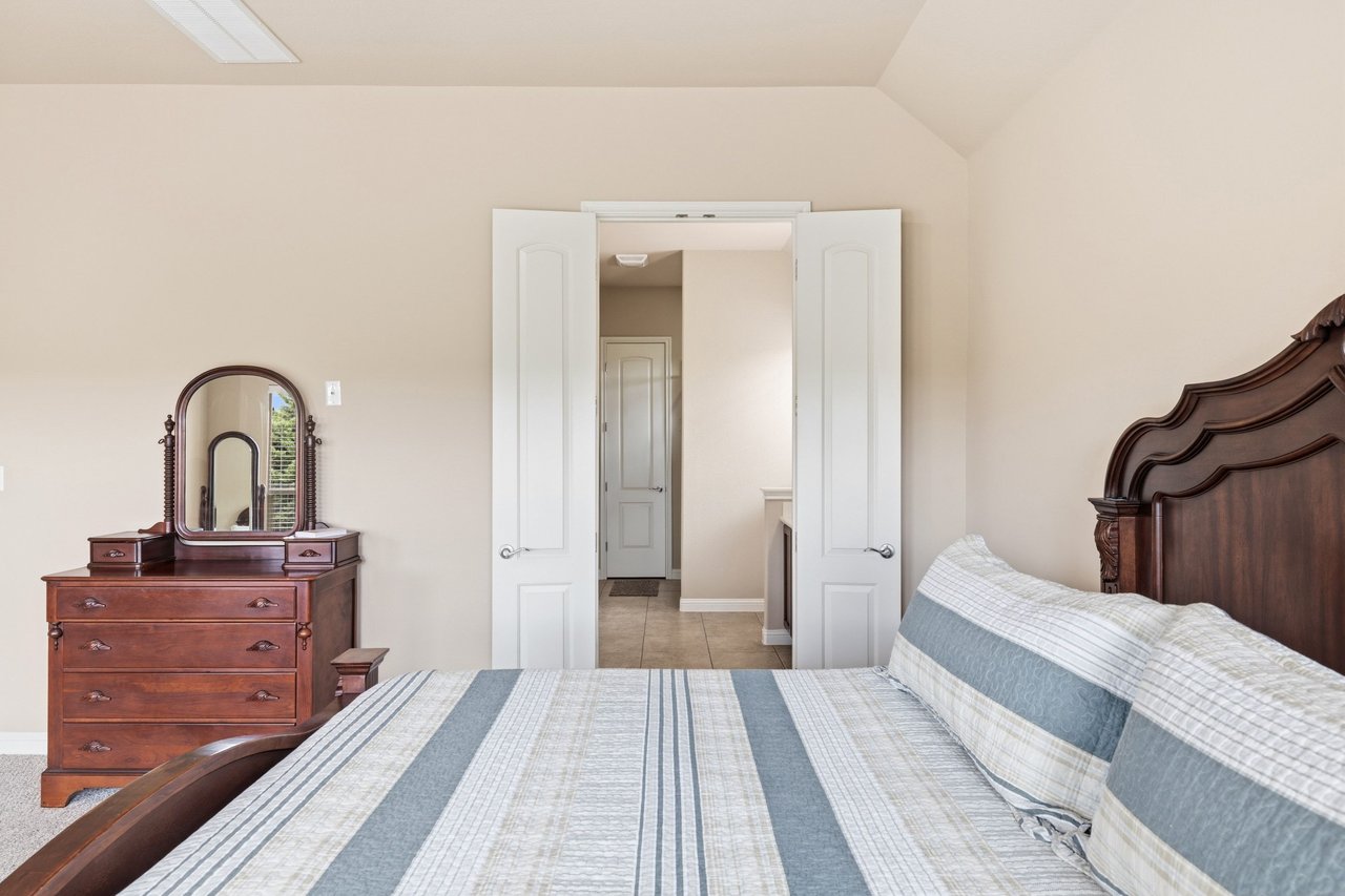 Bedroom with a blue-and-white striped bedspread, carved wooden headboard, and dresser with oval mirror.