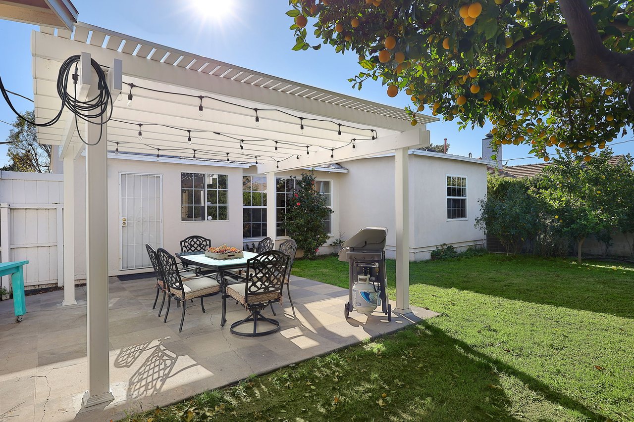 Outdoor dining setup under a white pergola with string lights, citrus trees, and barbecue grill at 17049 Baltar Street in Lake Balboa CA