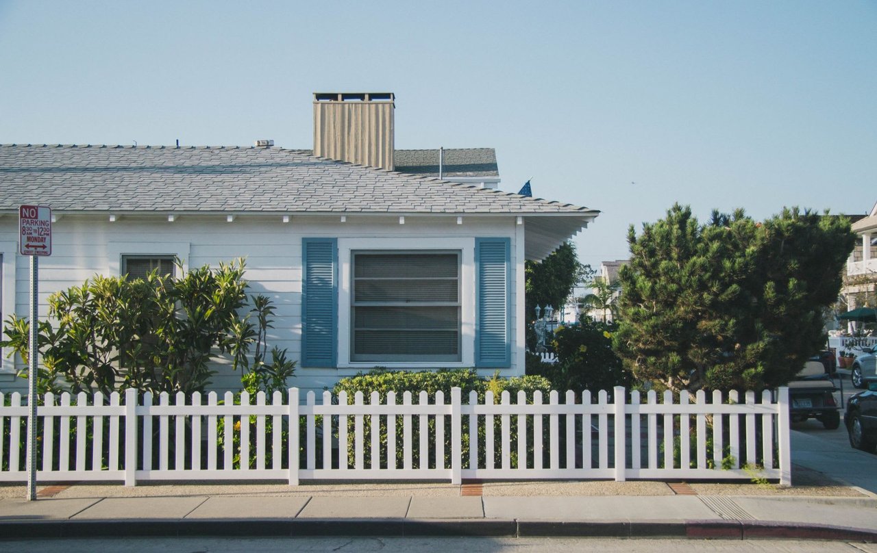  A bright, eye-level shot captures the front of a charming, single-story white house with a light grey shingled roof
