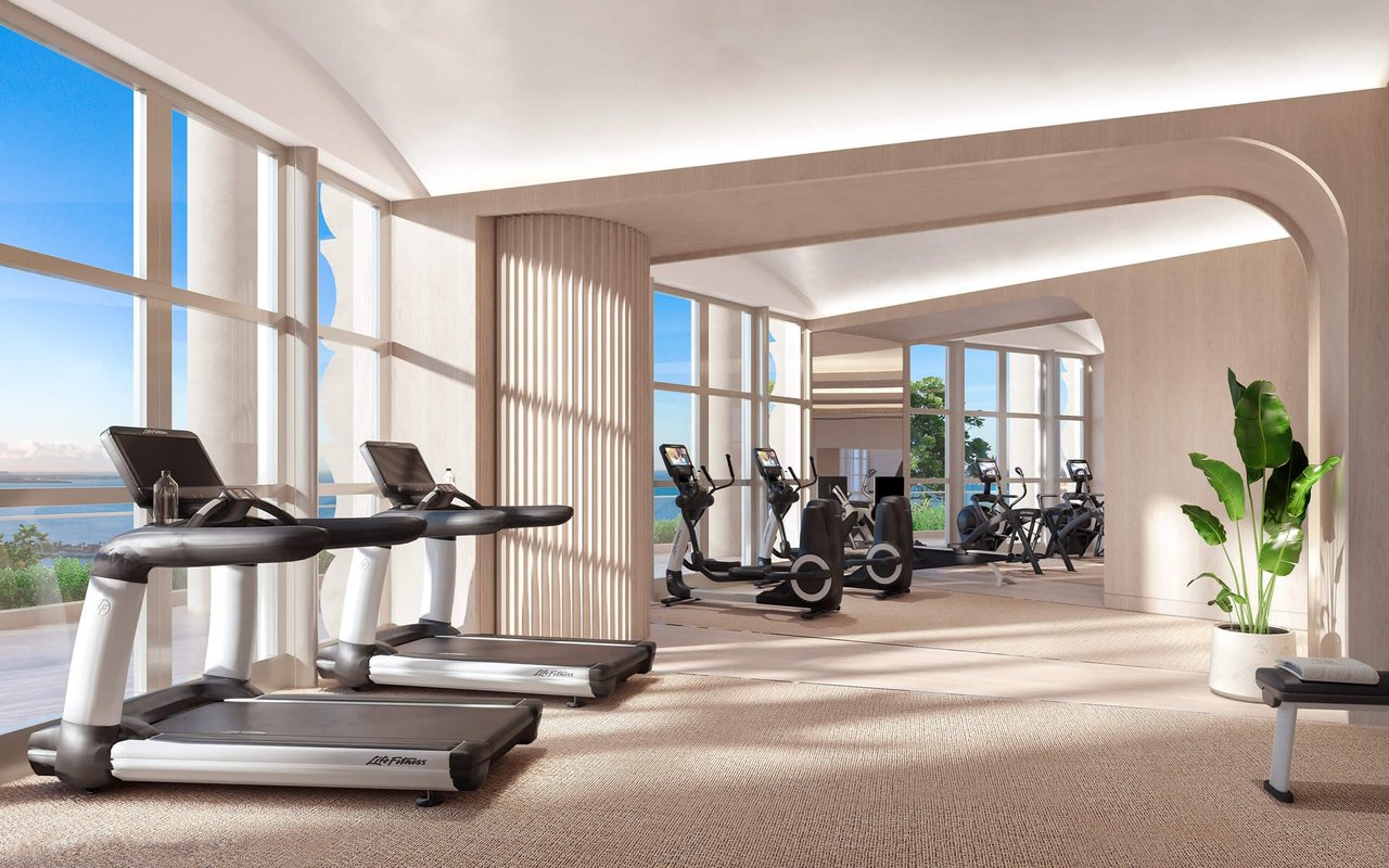 Residential fitness center with treadmills, cardio equipment, and floor-to-ceiling windows overlooking the water.